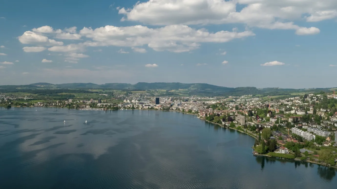 Aerial view of a Swiss city on a lake, surrounded by hills